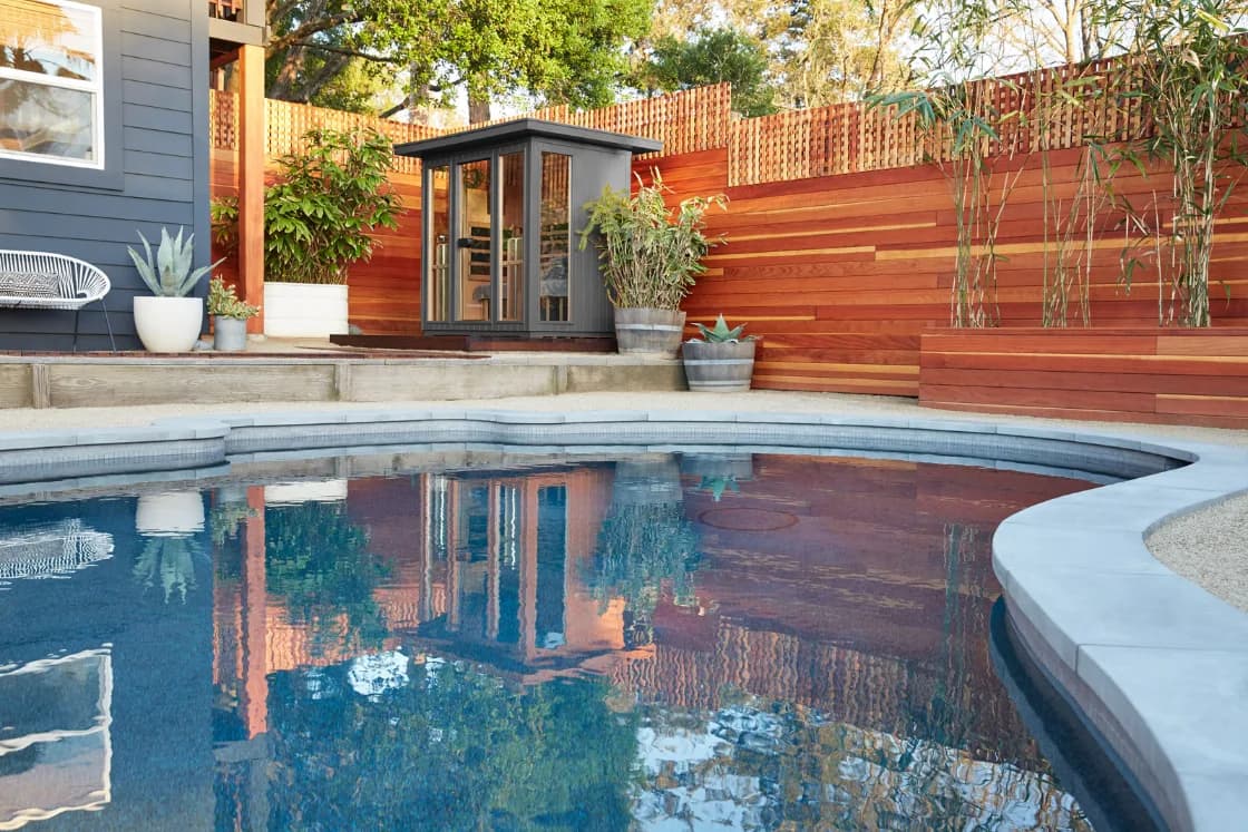 Clearlight's own image of a grey outdoor cabin tucked into the corner of a small backyard between the house and a redwood fence, beside a curved pool.