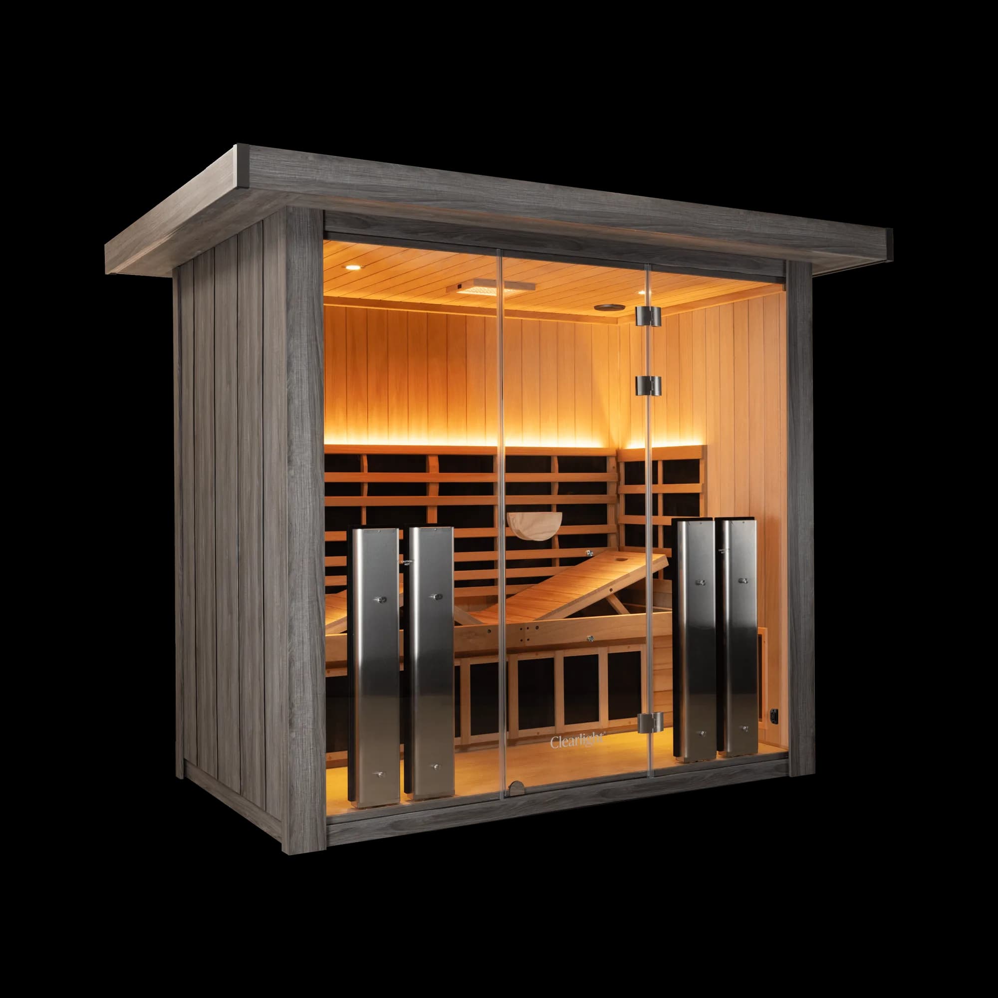 Clearlight Sanctuary Outdoor 5 infrared sauna from the front left corner, grey driftwood finish exterior and roof cap, glass front showing the lit interior, raised bench recliners and four heater towers