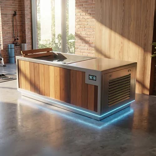 Finnmark SOULCOLD cold plunge in a bright room with a brick wall, cedar skirt, stainless top, side chiller panel and a blue light under the base