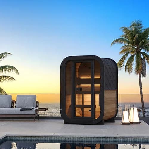 SaunaLife's rendering of a compact CL3G sauna on a poolside terrace above the ocean at sunset, palm trees, lanterns, and a lounge sofa beside it.