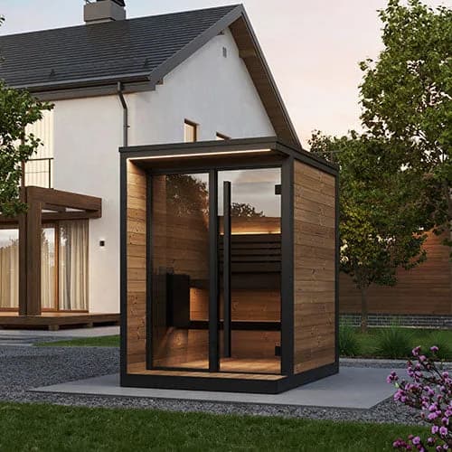 SaunaLife's rendering of the GL4 cabin sauna on a concrete slab beside a white house at dusk, its glass front lit warm from inside.