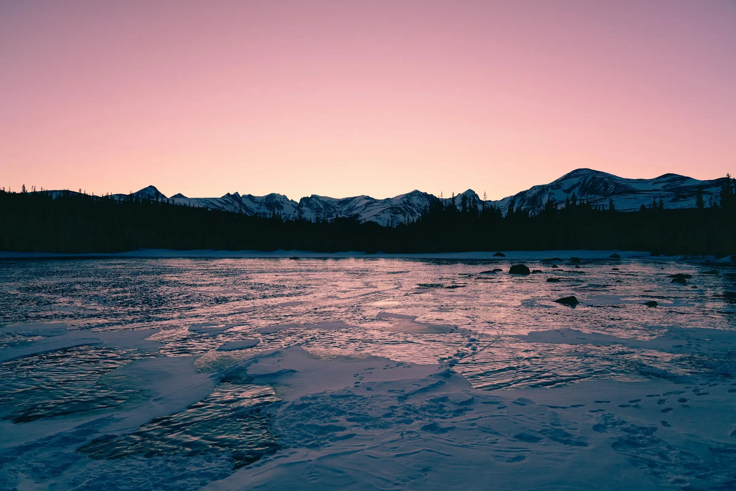 A lake at sunrise under a pink sky, with a mountain range along the far shore.