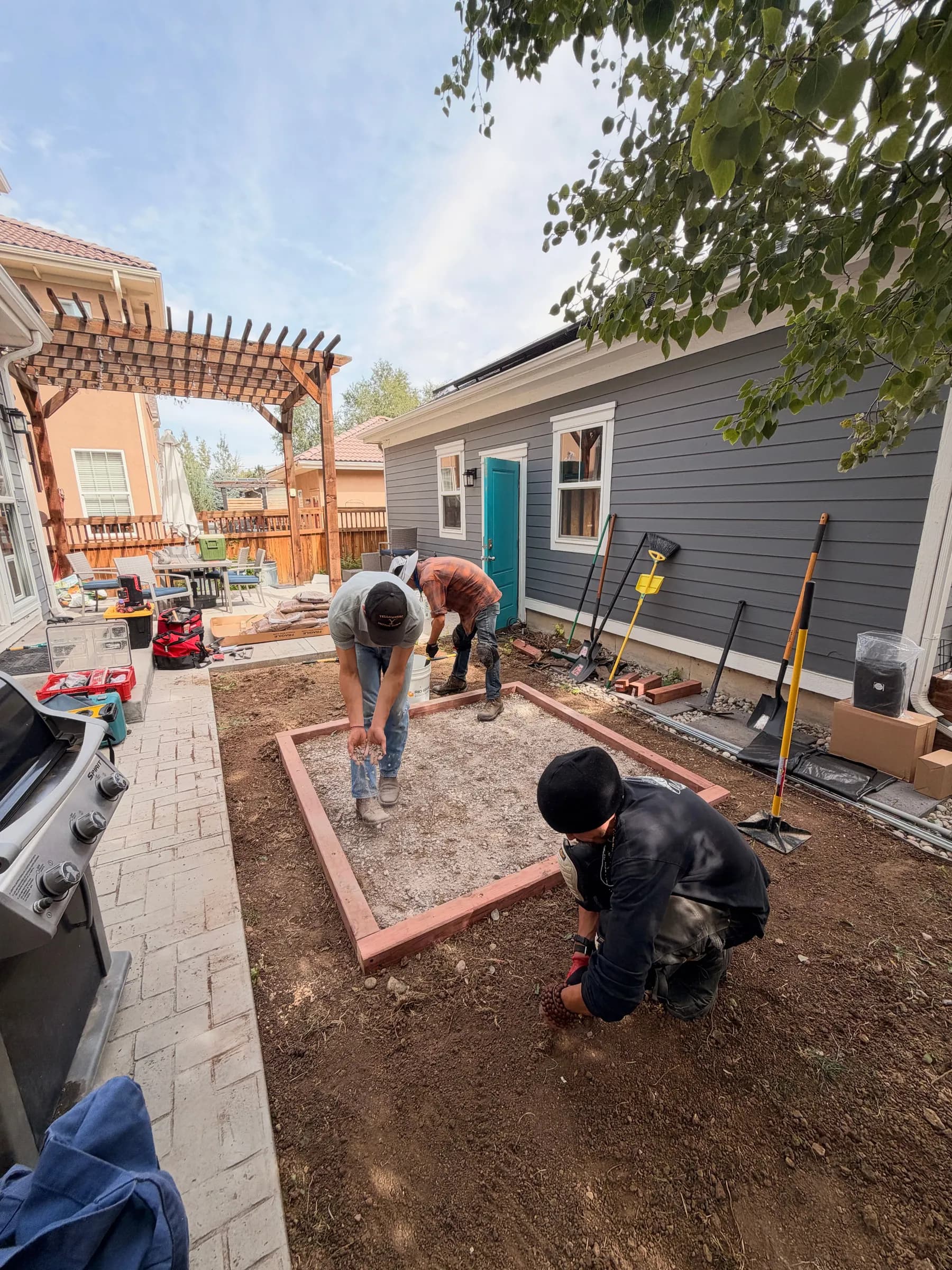 Our crew levelling a gravel pad inside a timber frame in a back yard, tools against the house and a pergola behind.