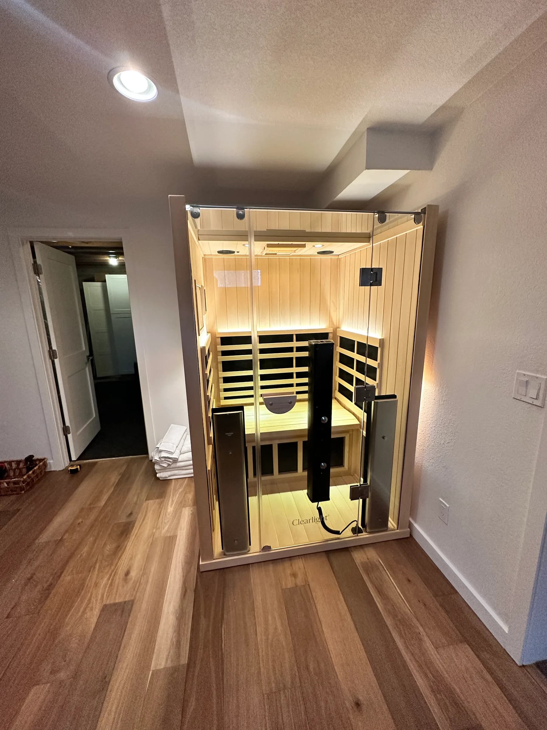 A Clearlight infrared cabin installed at the end of a finished hallway on a wood floor, lit from inside.